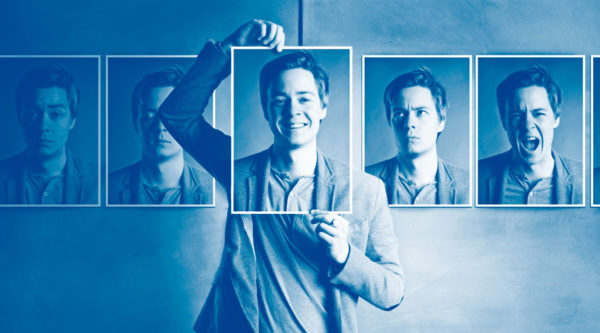 Person behind a row of pictures of faces, holding a picture of a smiling face