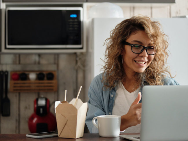 Number-one-question-blog Woman working from home on a laptop with a mug, a rice box, and her phone next to her.