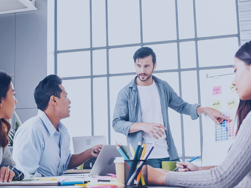 brand-strategist-skills-blog Meeting of four people, one stands and points to a whiteboard