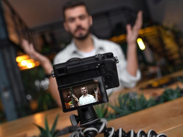 Man behind a camera on a tripod, recording video content of him speaking
