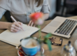 Person writing notes with a laptop and coffee in front of her.