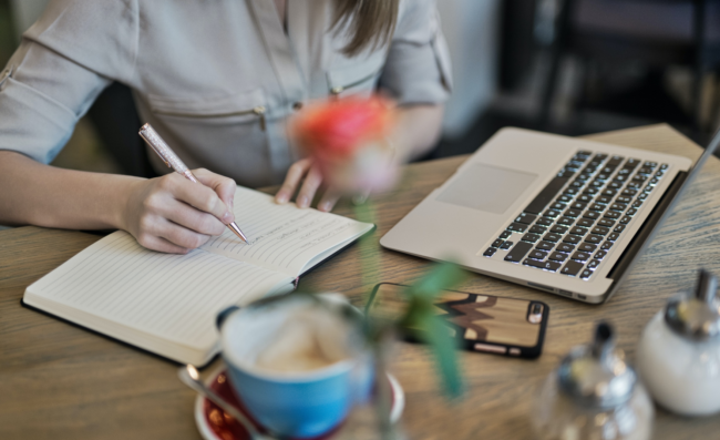 blog pic Person writing notes with a laptop and coffee in front of her.